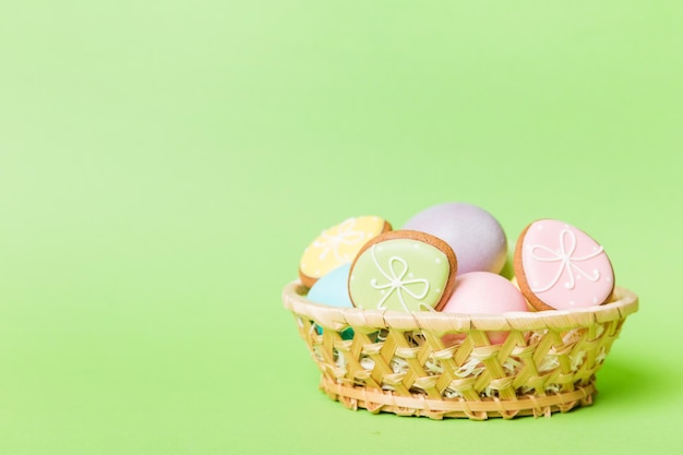 Galletas de Pascua coloridas en cesta con huevos de Pascua de varios colores sobre fondo de color Concepto de vacaciones de huevos de Pascua de color pastel con espacio de copia