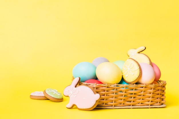 Galletas de Pascua coloridas en cesta con huevos de Pascua de varios colores sobre fondo de color Concepto de vacaciones de huevos de Pascua de color pastel con espacio de copia