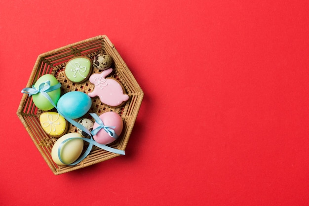 Galletas de Pascua coloridas en cesta con huevos de Pascua de varios colores sobre fondo de color Concepto de vacaciones de huevos de Pascua de color pastel con espacio de copia