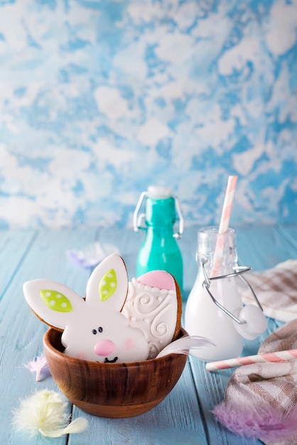 Galletas de Pascua como conejo y huevo en el cuenco de madera con leche en vidrio en el fondo de madera