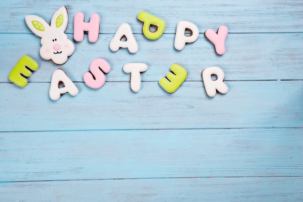 Foto galletas que ponen letras a pascua feliz con la tarjeta del conejo en fondo azul de madera.