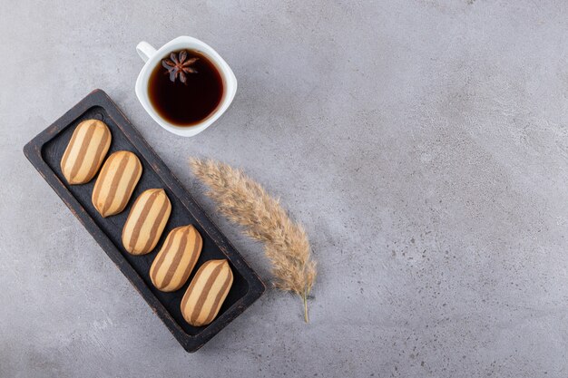 Galletas de rayas en tablero de madera oscura con taza de té.