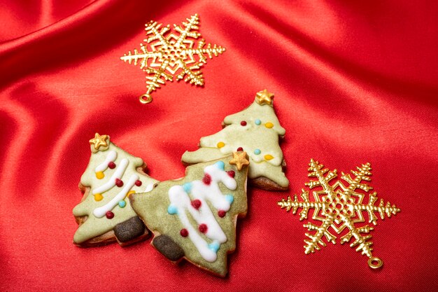 Galletas recubiertas de azúcar de árbol de pino de tema navideño en una tela de seda de color rojo brillante.