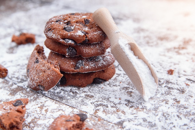 Galletas con rodajas de chocolate espolvoreadas con azúcar en polvo y una cuchara dosificadora de madera. Pastelería fresca en madera.