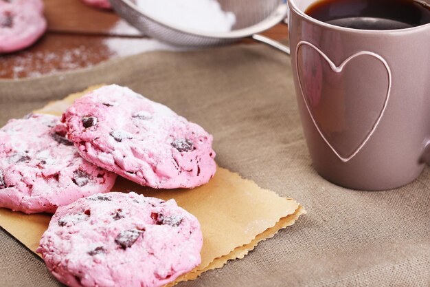 Galletas rosadas y taza de café en la mesa de madera