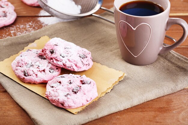 Galletas rosadas y taza de café en la mesa de madera