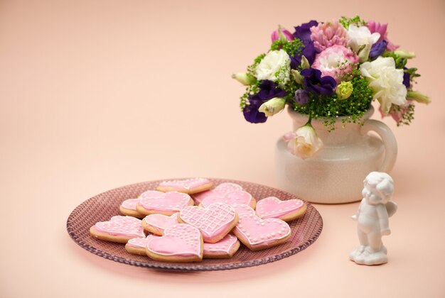 Galletas rosas en forma de corazones en un plato con ángeles y flores en el día de San Valentín