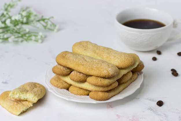 Galletas savoyardi galletas, café y flores sobre una superficie de mármol blanco