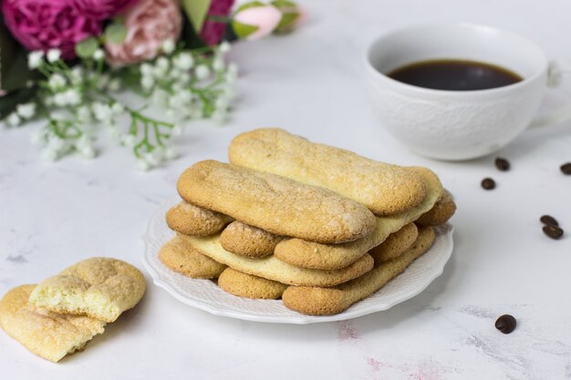 Galletas savoyardi galletas, café y flores sobre una superficie de mármol blanco