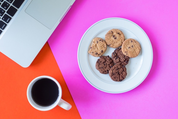 Foto galletas con la taza de café y la computadora portátil en fondo colorido.