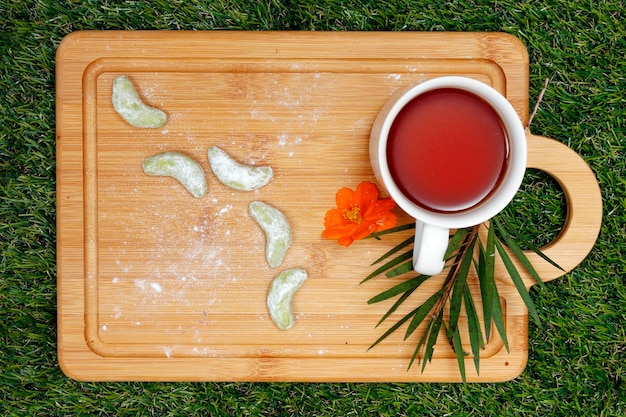 Galletas de té verde y taza de té en bandeja de madera