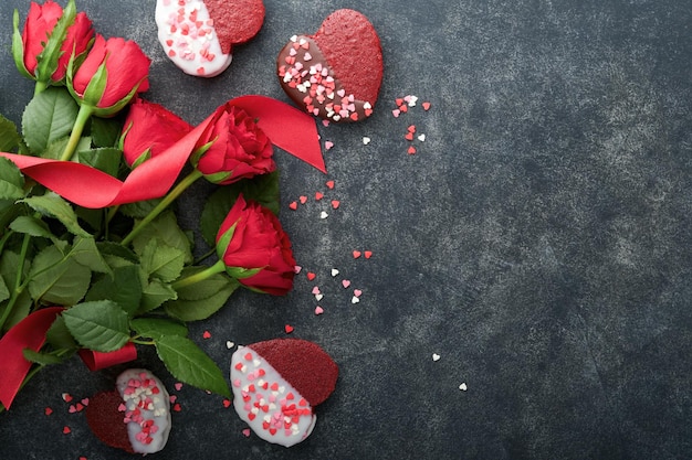 Galletas de terciopelo rojo o brownie en forma de corazón con glaseado de chocolate con rosas rojas sobre fondo negro Idea de postre para el Día de San Valentín Día de la Madre o de la Mujer Postre casero Pastel para el Día de San Valentín
