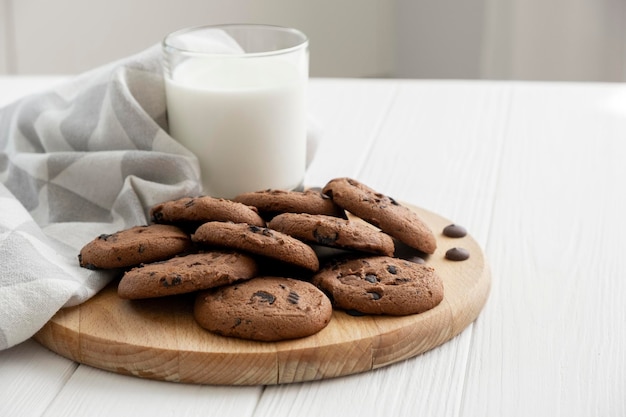 Galletas con trocitos de chocolate caseras en una tabla de madera con un vaso de leche y un paño de cocina Receta de galletas de avena con trocitos de chocolate Variante del desayuno matutino