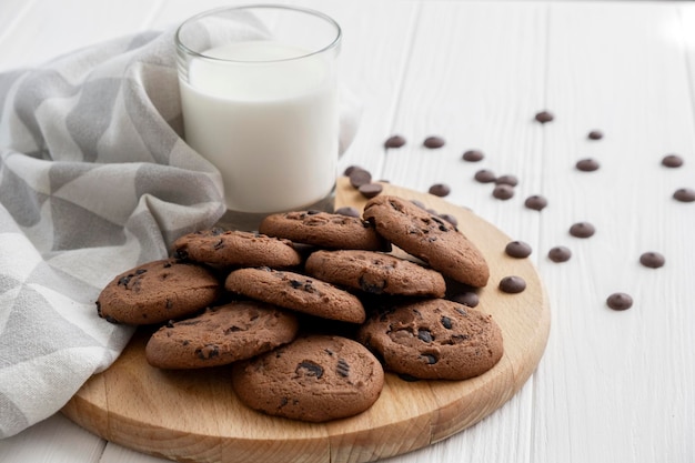 Galletas con trocitos de chocolate caseras en una tabla de madera con un vaso de leche y un paño de cocina Receta de galletas con trocitos de chocolate Merienda o golosina para el té o el café