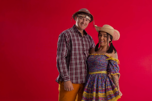 Foto gama distrito federal brasil 29 de maio de 2022 jovem casal vestindo trajes festivos em foto de estúdio com fundo vermelho e poses divertidas festa junina brasil