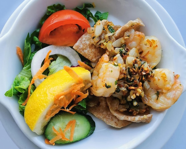 Gambas al ajillo con ensalada de verduras y limón en un bol blanco