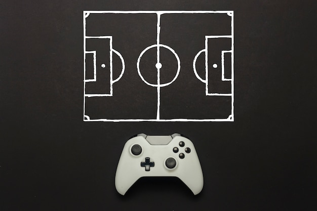 Gamepad blanco sobre un fondo negro. Se agregó un esquema de campo de fútbol. Tácticas del juego. Concepto de juego de fútbol en la consola, juegos de computadora. Vista plana, vista superior.