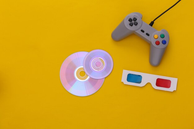 Gamepad retro e CD, óculos 3D em fundo amarelo. Vista do topo