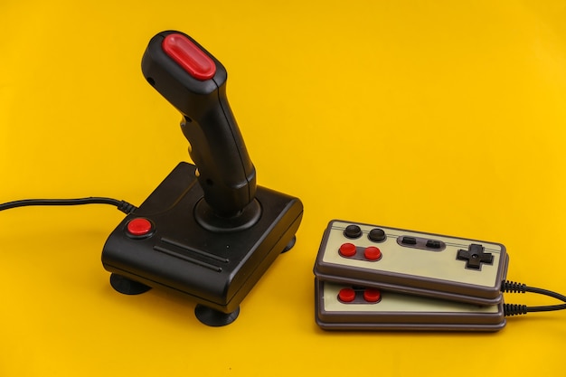 Gamepads retrô e joystick em fundo amarelo. Videogame, jogos dos anos 80.