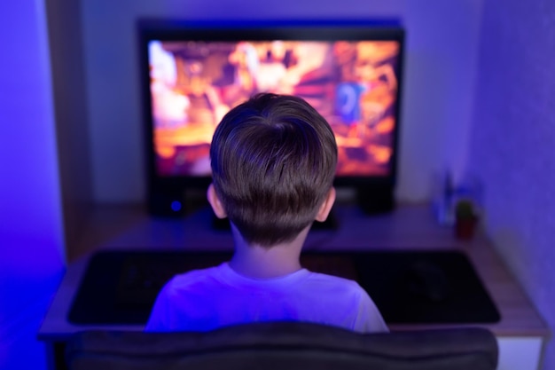 Gamer boy jugando videojuegos en línea en una computadora en una habitación oscura