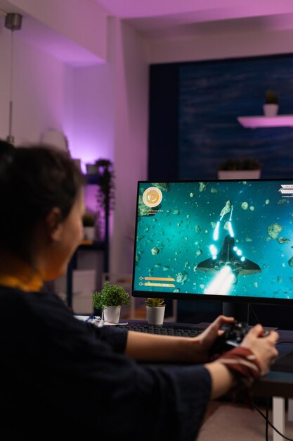 Gamer jugando videojuegos con joystick en el monitor. Mujer alegre con controlador para jugar juegos en línea en internet. Jugador haciendo una actividad divertida en el ciberespacio con equipos de juego.