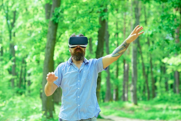 Gamer man usa gafas VR en el bosque de verano Gamer juega un juego de realidad virtual con un dispositivo móvil al aire libre