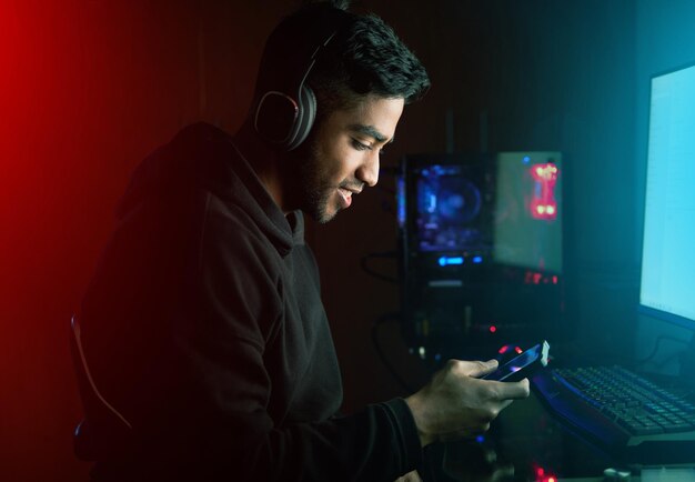 Gamer-Mann und Texting mit Telefon mit in der Nacht Lächeln oder Lesen für Einladung Link zu RPG-Wettbewerb Person Smartphone und Pro-Gaming mit Chat-Herausforderung und Esports-App durch Computer im dunklen Zuhause