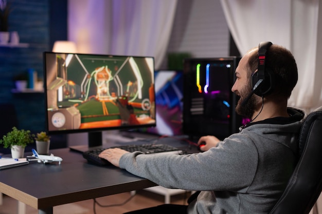 Gamer mit Headset, der Videospiele auf dem Computer spielt. Mann mit Kopfhörern, der Tastatur und Mauspad verwendet, um Online-Videospiele auf dem Monitor mit Spielgeräten zu spielen. Moderner Spieler