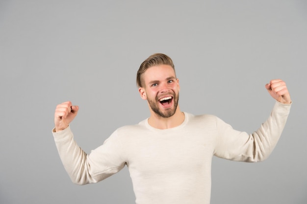 Ganador alegre. Hombre feliz rostro alegre posando con músculos como ganador. Guy celebra la victoria. Dulce sabor a gloria. Hombre exitoso guapo sin afeitar macho elegante, fondo gris.