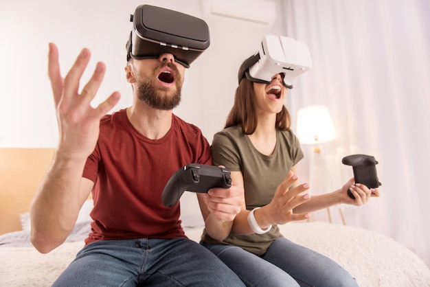 Ganador y perdedor. Enérgica pareja entusiasta optimista sosteniendo joysticks mientras usa gafas VR y gritando