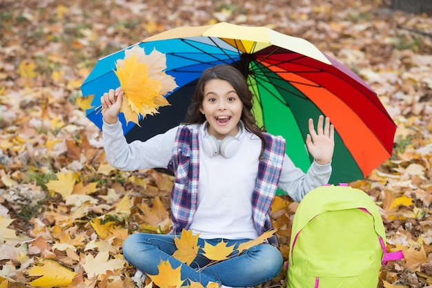 Ganador de todos los días niño de otoño bajo un paraguas colorido siente la inspiración infancia feliz regreso a la escuela niña con mochila en el parque disfruta del otoño en el bosque niño reúne hojas de arce caídas amarillas
