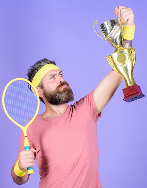 Ganar el juego de tenis Ganador del partido de tenis Logró el mejor jugador de tenis ganar el campeonato El atleta sostiene la raqueta de tenis y la copa de oro El hombre barbudo hipster usa ropa deportiva Éxito y logro