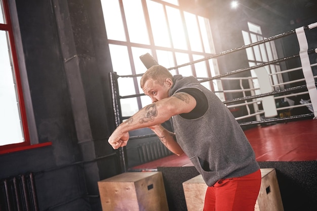 Gancho de direita, atleta bonito e confiante em roupas esportivas boxe com sombra em pé do lado oposto