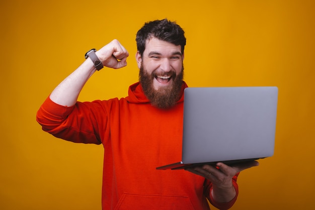 Gané. La foto de un joven barbudo muestra el gesto del ganador mientras mira su computadora portátil que tiene.