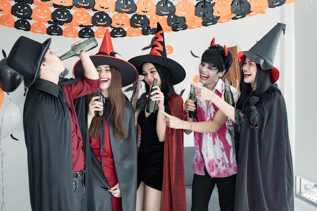 Gangue de jovem asiático fantasiado de bruxa, feiticeiro e festa de halloween para dançar e beber e bêbado no quarto. grupo adolescente tailandês com celebrar o halloween. festa de halloween do conceito em casa.