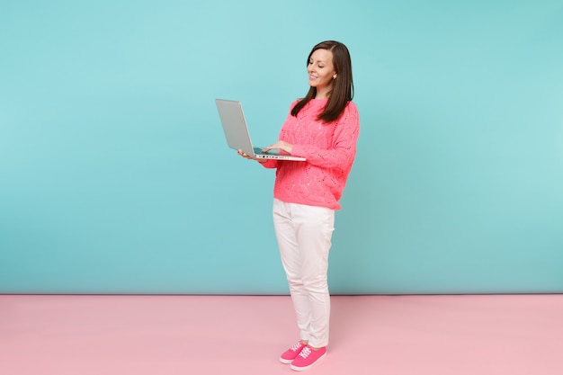 Ganzaufnahme der Frau in gestricktem Rosenpullover, weiße Hose mit Laptop-PC