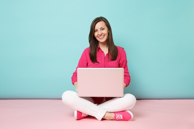 Ganzaufnahme der jungen Frau in rosa Hemdbluse weiße Hose, die mit Laptop-PC auf dem Boden sitzt