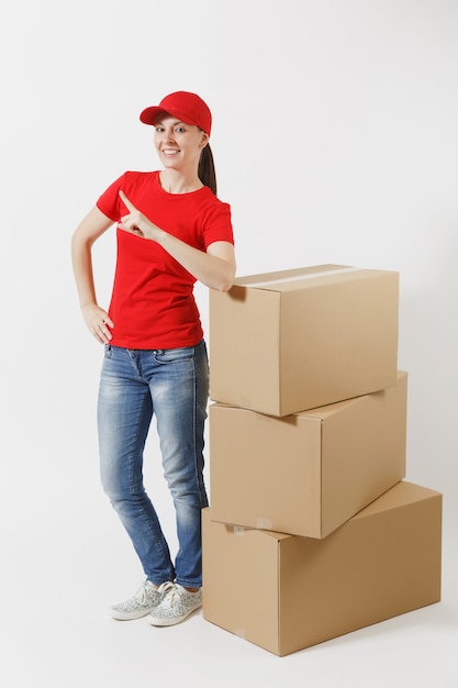 Ganzaufnahme der Lieferfrau in der roten Kappe, T-Shirt lokalisiert auf weißem Hintergrund. Weiblicher Kurier oder Händler, der in der Nähe von leeren Kartons steht. Paket empfangen. Kopieren Sie Platz für Werbung.