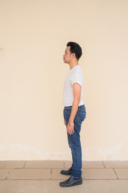 Ganzaufnahme des asiatischen Mannes mit weißem T-Shirt vor einfarbigem Hintergrund im Freien