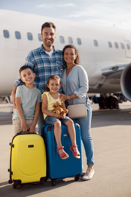 Ganzaufnahme einer glücklichen vierköpfigen Familie, die tagsüber vor einem großen Flugzeug steht und in die Kamera lächelt. Menschen, Reisen, Urlaubskonzept