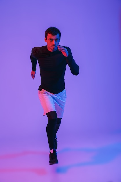 Ganzaufnahme eines fitten Sportlers, der isoliert über violette Wand läuft