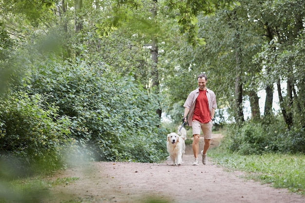 Ganzaufnahme eines glücklichen erwachsenen Mannes, der Hund im grünen Park im Sommerkopierraum spazieren geht