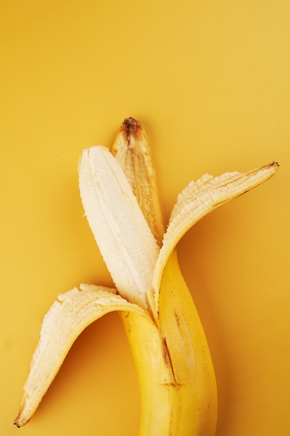 Ganze halb geschälte Banane isoliert auf gelbem Hintergrund Nahaufnahme