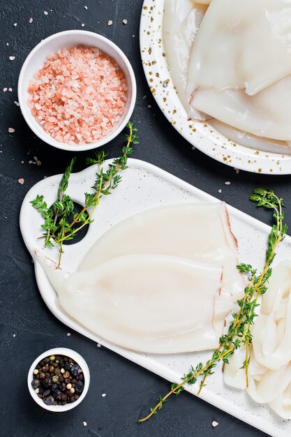 Ganze rohe Tintenfische und in Ringe schneiden auf einem Schneidebrett Zutaten zum Kochen Thymian, Pfeffer, rosa Salz