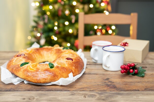 Ganze Roscón de Reyes auf Holztisch mit Weihnachtsbaum im Hintergrund. Weihnachtssüßigkeiten.