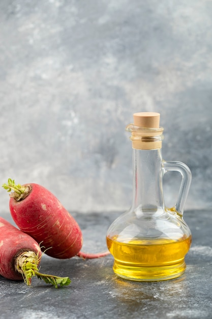 Ganze rote radieschen mit einer glasflasche öl auf einem marmortisch.