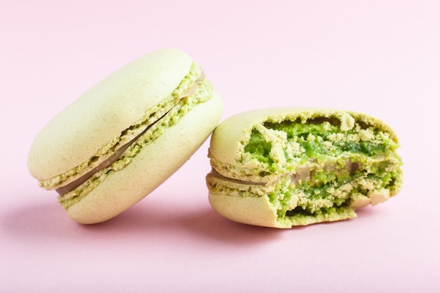 Ganze und gebissene grüne Macarons oder Makronen backen auf Pastellrosahintergrund zusammen