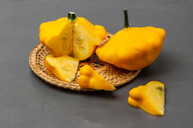 Ganze und geschnittene gelbe Zucchini auf einem Weidenteller Zucchinischeiben auf dem Tisch