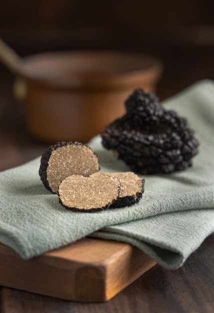 Ganze und geschnittene schwarze Trüffelpilze auf Holzbrett auf grüner Serviette hautnah