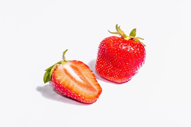 Ganze und halbe reife Erdbeere isoliert auf weißem Hintergrund. Süße frische Sommerfrüchte, gesundes Essen. Ein modernes hartes Licht, dunkler Schatten